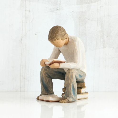 Willow Tree 'Quest' Figurine. A male figure seated on a stack of books with a book open at his feet, and another open in his hand as he leans over it reading.