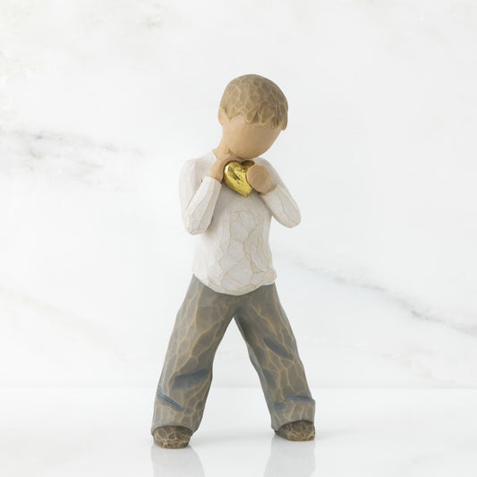A young boy holding a golden heart close to their chest.