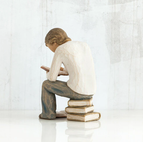 Willow Tree 'Quest' Figurine. A male figure seated on a stack of books with a book open at his feet, and another open in his hand as he leans over it reading.