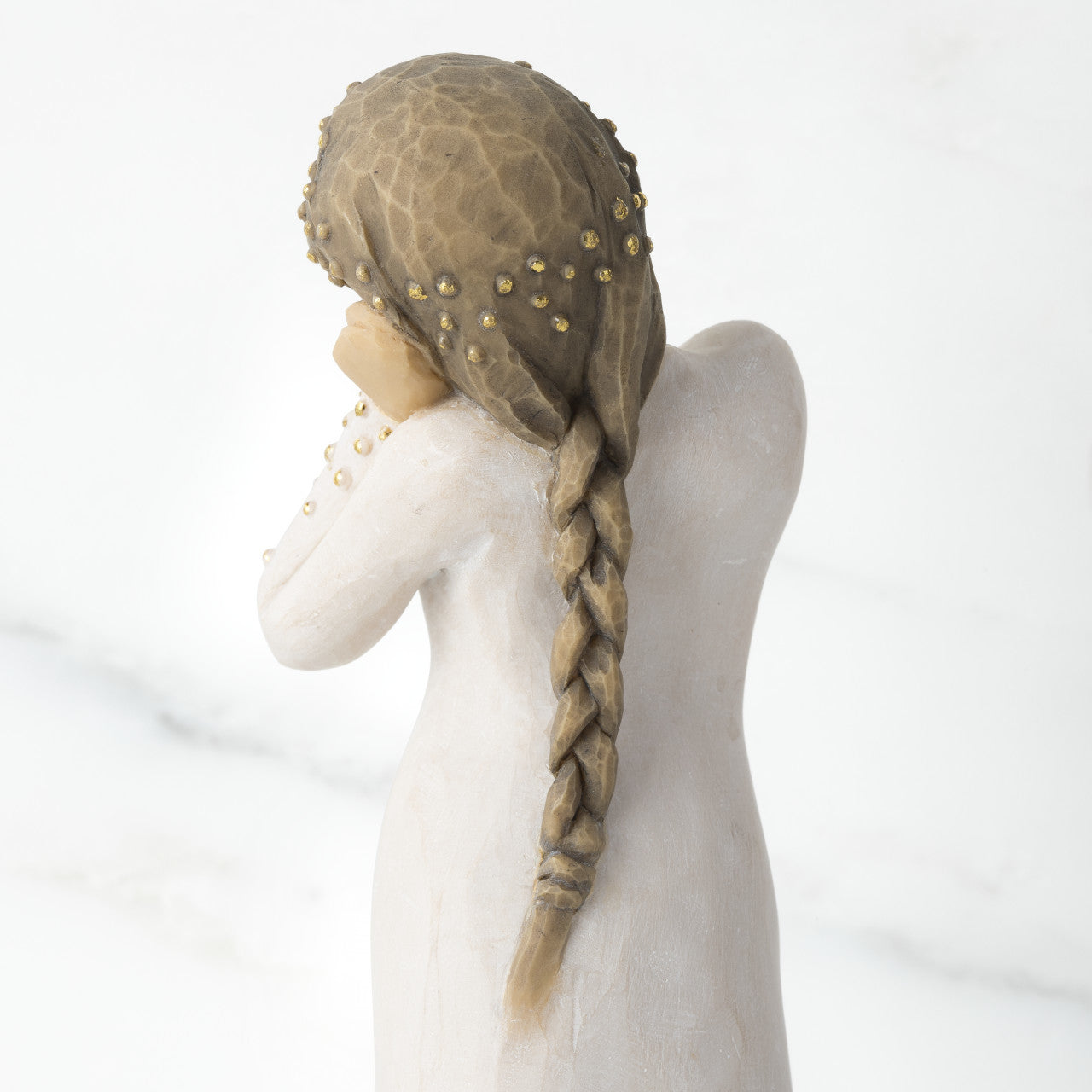The plaited hair and gold details on the back of the Willow Tree 'Wishing' Figurine. A female figure with tilted head resting on clasped hands, a hand-painted resin with applied gold leaf detail.